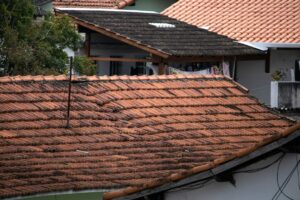 A homeowner examines damaged shingles and roof flashing from the ground beside a house.