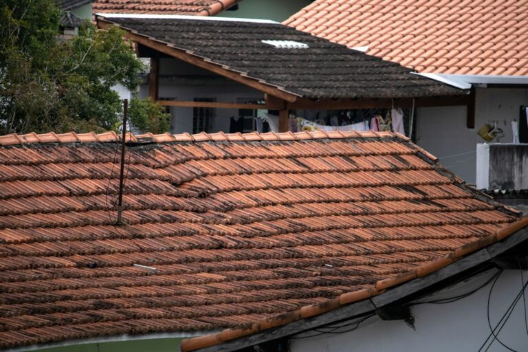 A homeowner examines damaged shingles and roof flashing from the ground beside a house.