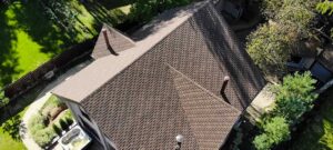 Sunlit residential roof with faded shingles, exposed granules, and a nearby gutter containing roofing debris.